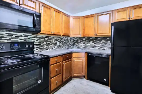 kitchen featuring electric range oven, refrigerator, dishwasher, stainless steel microwave, dark countertops, light hardwood flooring, and brown cabinets