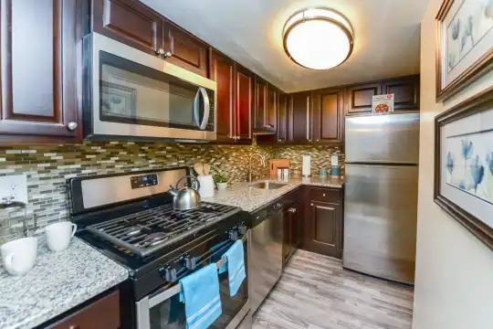 kitchen with stainless steel microwave, gas range oven, dishwasher, refrigerator, dark brown cabinetry, pendant lighting, light stone countertops, and light hardwood flooring