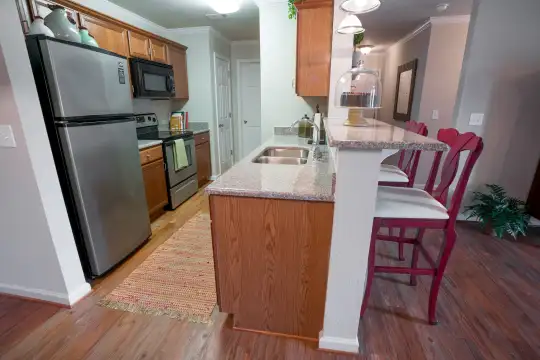 kitchen featuring a breakfast bar, stainless steel refrigerator, electric range oven, microwave, dark countertops, light hardwood flooring, and brown cabinetry