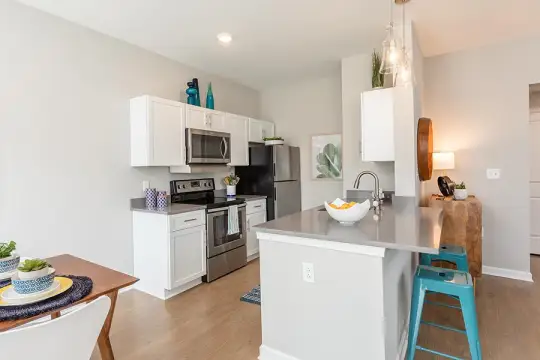 kitchen featuring refrigerator, electric range oven, stainless steel microwave, dark countertops, light hardwood flooring, pendant lighting, and white cabinets