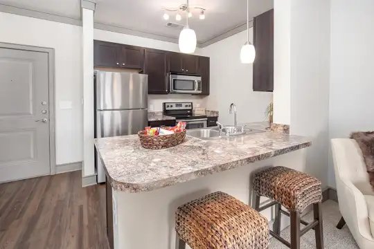 kitchen featuring a kitchen breakfast bar, stainless steel appliances, granite-like countertops, dark brown cabinetry, pendant lighting, and dark hardwood flooring
