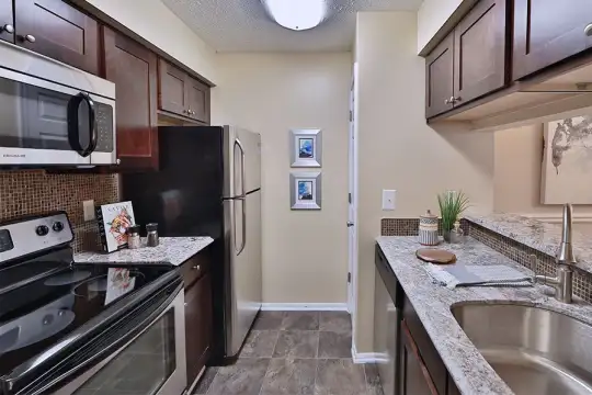 kitchen featuring stainless steel microwave, electric stovetop, refrigerator, dishwasher, stone countertops, dark tile flooring, and dark brown cabinets