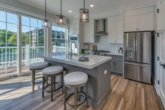 kitchen with a healthy amount of sunlight, a breakfast bar area, stainless steel appliances, ventilation hood, white cabinetry, light countertops, kitchen island sink, light floors, and pendant lighting