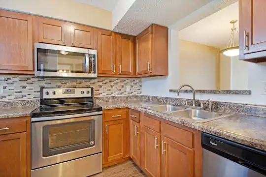 kitchen with electric range oven, stainless steel appliances, granite-like countertops, brown cabinetry, and light parquet floors