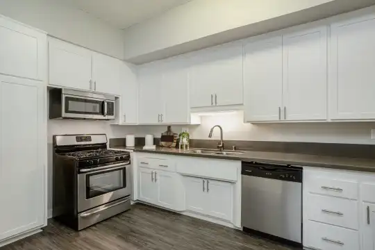 kitchen featuring stainless steel appliances, gas range oven, white cabinetry, dark countertops, and dark hardwood flooring