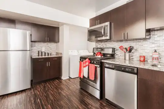 kitchen with washer / dryer, gas range oven, stainless steel appliances, dark brown cabinetry, light stone countertops, and dark hardwood flooring