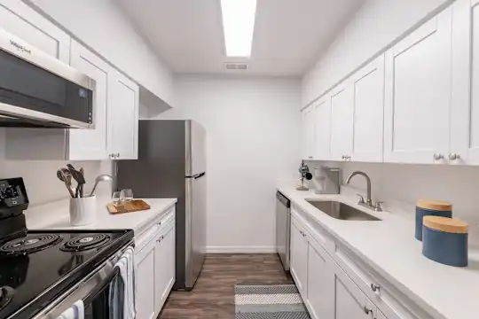 kitchen featuring refrigerator, dishwasher, microwave, white cabinets, light countertops, and dark hardwood flooring