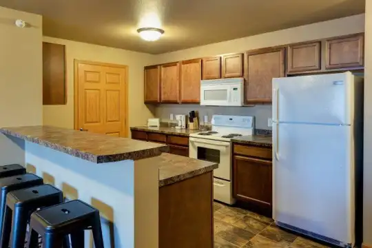 kitchen featuring a kitchen bar, refrigerator, electric range oven, microwave, dark stone countertops, dark tile flooring, and brown cabinets