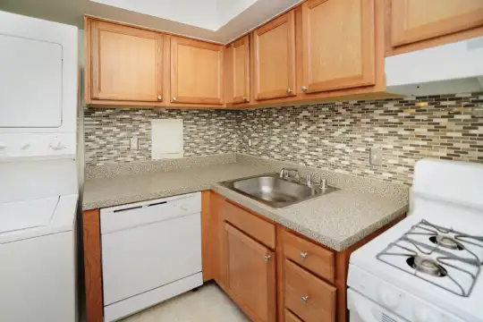 kitchen featuring washer / dryer, dishwasher, exhaust hood, light countertops, light tile floors, and brown cabinetry