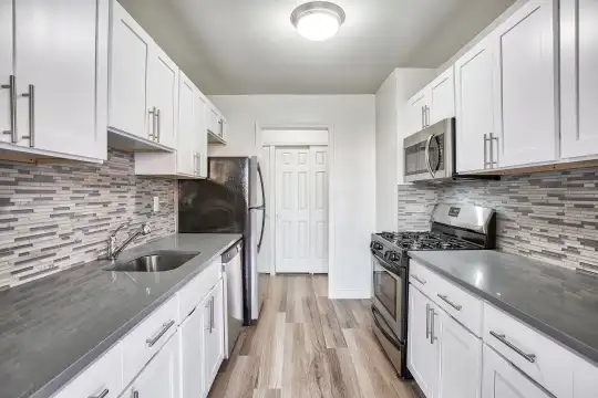 kitchen with gas range oven, dishwasher, stainless steel microwave, light hardwood flooring, white cabinets, and dark stone countertops