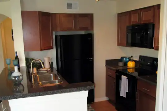 kitchen featuring refrigerator, electric range oven, microwave, dark flooring, dark stone countertops, and dark brown cabinets