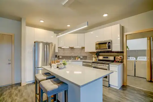 kitchen featuring a center island, a kitchen breakfast bar, stainless steel appliances, gas range oven, independent washer and dryer, white cabinetry, pendant lighting, light parquet floors, and light countertops