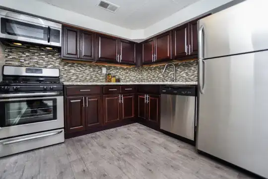 kitchen with stainless steel appliances, gas range oven, stone countertops, dark brown cabinetry, and light parquet floors