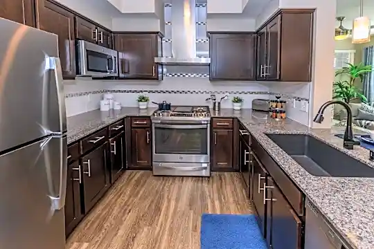 kitchen featuring range oven, ventilation hood, stainless steel appliances, dark brown cabinets, pendant lighting, light hardwood floors, and dark stone countertops