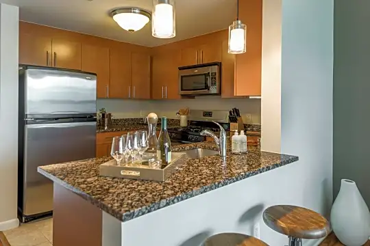 kitchen with a breakfast bar, stainless steel appliances, range oven, brown cabinetry, dark granite-like countertops, light tile floors, and pendant lighting