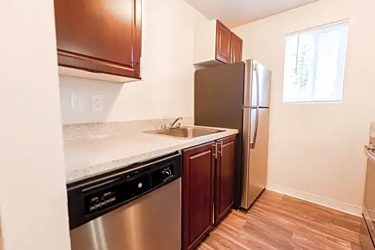 kitchen featuring natural light, refrigerator, stainless steel dishwasher, range oven, dark brown cabinets, light stone countertops, and light hardwood flooring