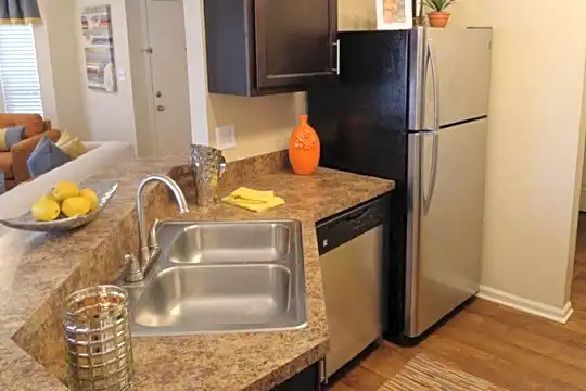 kitchen featuring natural light, refrigerator, dishwasher, dark brown cabinetry, dark countertops, and light hardwood flooring