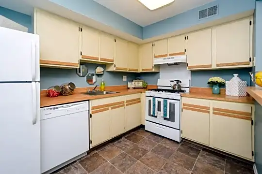 kitchen featuring range hood, refrigerator, dishwasher, gas range oven, light countertops, dark tile floors, and white cabinetry