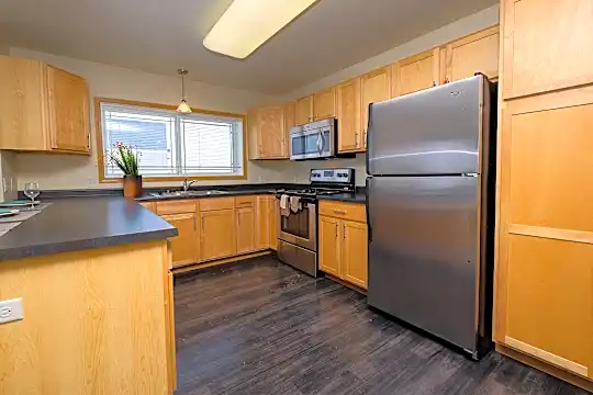 kitchen featuring natural light, stainless steel appliances, range oven, dark countertops, pendant lighting, dark hardwood flooring, and brown cabinets