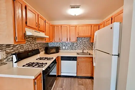 kitchen featuring gas range oven, range hood, dishwasher, refrigerator, microwave, light countertops, brown cabinets, and light hardwood flooring