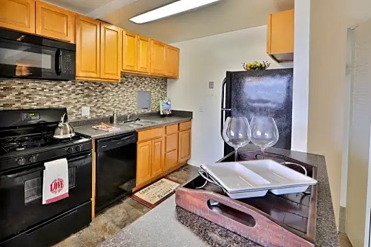 kitchen featuring refrigerator, gas range oven, dishwasher, microwave, dark granite-like countertops, and brown cabinets