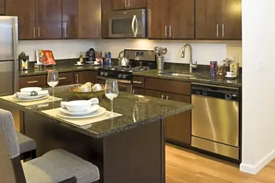 kitchen with a kitchen bar, range oven, stainless steel appliances, dark brown cabinets, dark countertops, and light hardwood flooring