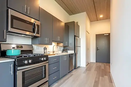 kitchen featuring stainless steel microwave, gas range oven, dishwasher, refrigerator, light countertops, dark brown cabinets, and light hardwood flooring