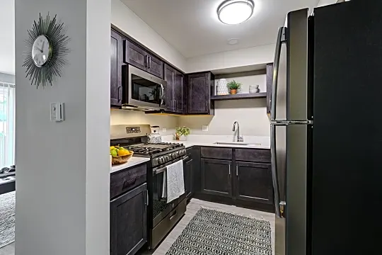 kitchen featuring refrigerator, gas range oven, microwave, light flooring, dark brown cabinetry, and light countertops