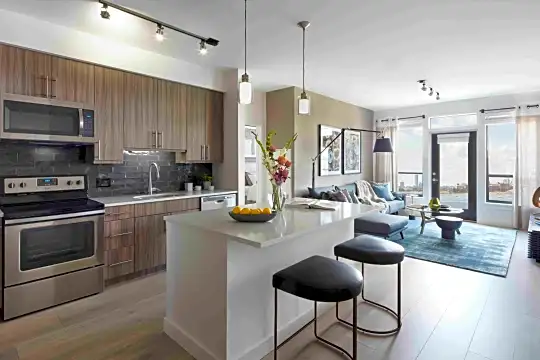 kitchen featuring a kitchen breakfast bar, stainless steel microwave, electric range oven, dishwasher, brown cabinets, light countertops, light parquet floors, pendant lighting, and a kitchen island with sink