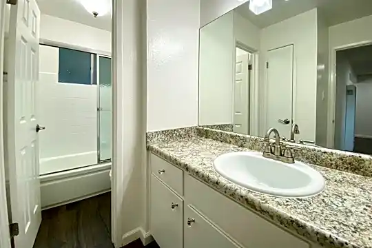 bathroom featuring hardwood flooring, enclosed tub / shower combo, mirror, and vanity