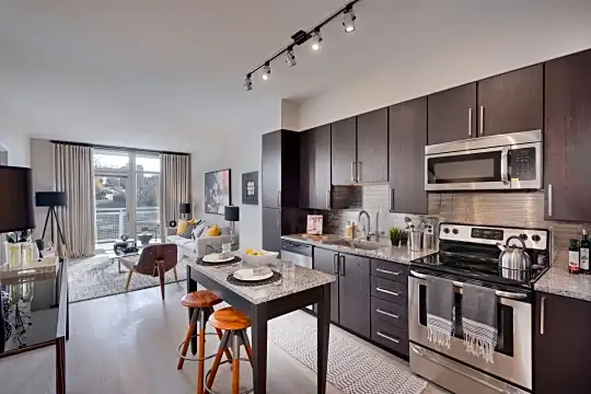 kitchen featuring natural light, electric range oven, stainless steel microwave, TV, dark brown cabinetry, light granite-like countertops, and light flooring