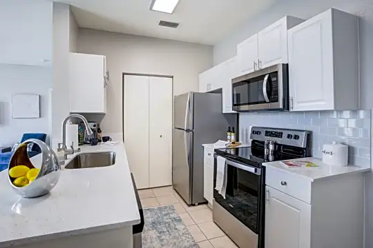 kitchen with stainless steel microwave, refrigerator, electric range oven, white cabinetry, light countertops, and light tile floors