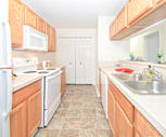 kitchen featuring electric range oven, refrigerator, dishwasher, microwave, light tile flooring, light countertops, and brown cabinetry, South Pointe Apartments