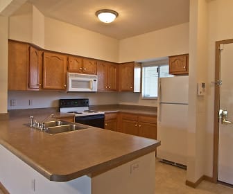 kitchen with natural light, refrigerator, electric range oven, microwave, light tile flooring, brown cabinets, and light countertops, Steeplechase Apartments & Townhomes