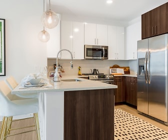 kitchen featuring natural light, a breakfast bar area, stainless steel appliances, range oven, light countertops, kitchen island sink, light parquet floors, pendant lighting, and dark brown cabinets, The Cynwyd