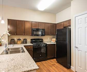 kitchen with gas range oven, refrigerator, microwave, dark brown cabinetry, pendant lighting, light stone countertops, and light parquet floors, Estate at Woodmen Ridge