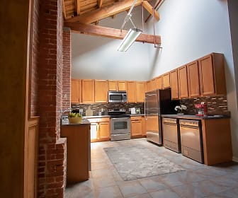 kitchen featuring a high ceiling, wood beam ceiling, stainless steel appliances, range oven, dark countertops, light tile flooring, and brown cabinets, Spinnaker Station