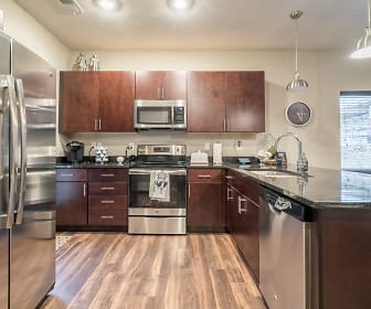 kitchen with natural light, electric range oven, stainless steel appliances, dark brown cabinetry, dark granite-like countertops, pendant lighting, and light hardwood flooring, The Villas at Falling Waters