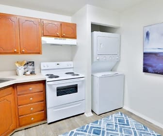 kitchen with exhaust hood, washer / dryer, refrigerator, electric range oven, light tile floors, light countertops, and brown cabinetry, Towson Crossing Apartment Homes