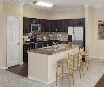 kitchen with a kitchen bar, a kitchen island, electric range oven, stainless steel appliances, dark countertops, dark brown cabinets, and light parquet floors, Camden Riverwalk Apartments