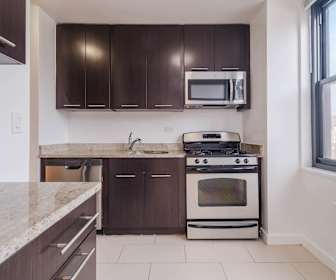 kitchen with natural light, stainless steel microwave, radiator, gas range oven, dishwasher, light tile floors, light granite-like countertops, and dark brown cabinets, 303 East 83rd