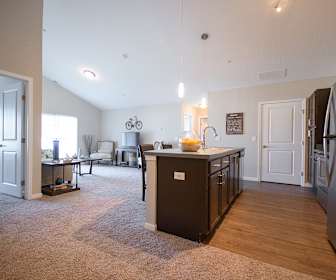 kitchen with carpet, vaulted ceiling, natural light, refrigerator, TV, range oven, light floors, dark brown cabinetry, kitchen island sink, and pendant lighting, The Boulevard at Green