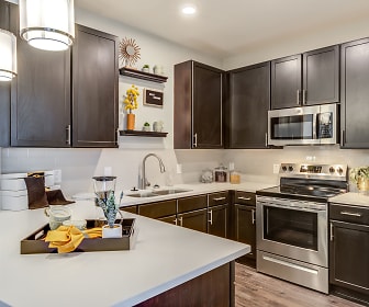 kitchen with stainless steel appliances, electric range oven, light countertops, pendant lighting, dark brown cabinetry, and light hardwood floors, The Grove at Carolina Park