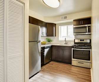 kitchen featuring natural light, stainless steel microwave, gas range oven, dishwasher, refrigerator, dark brown cabinetry, light stone countertops, and light hardwood flooring, Glen Ridge Apartment Homes