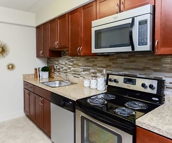 kitchen with stainless steel microwave, electric range oven, dishwasher, brown cabinets, light tile flooring, and light stone countertops, Stonegate at Devon