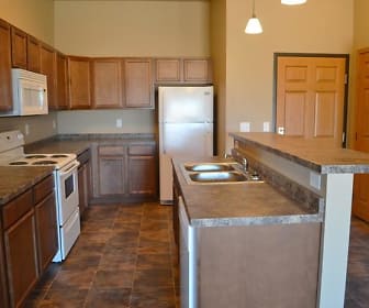 kitchen featuring a center island, refrigerator, electric range oven, dishwasher, microwave, dark stone countertops, dark tile floors, pendant lighting, and brown cabinetry, Stanley ND Apartments