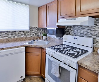 kitchen featuring ventilation hood, gas range oven, dishwasher, refrigerator, microwave, stone countertops, dark flooring, and brown cabinetry, Princeton Estates