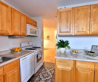 kitchen with gas range oven, dishwasher, microwave, dark flooring, light countertops, and brown cabinetry, The Carlyle Apartment Homes