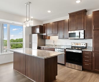 kitchen featuring a kitchen island, natural light, stainless steel microwave, refrigerator, electric range oven, dishwasher, dark brown cabinetry, pendant lighting, light stone countertops, and light hardwood flooring, Sonder Point Senior Living