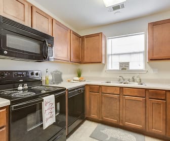 kitchen featuring natural light, electric range oven, refrigerator, dishwasher, microwave, light tile flooring, brown cabinets, and light countertops, Northbrook Apartments